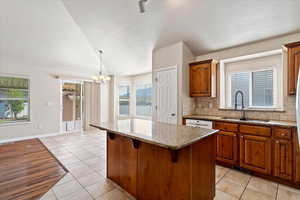 Kitchen featuring backsplash, wood finish cabinets, light tile patterned floors, light stone counters, and a kitchen island