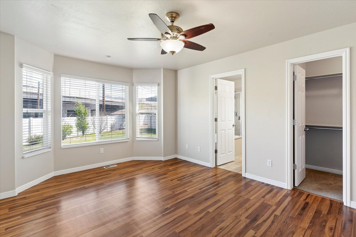 Primary Bedroom featuring a walk in closet, dark wood-type flooring, and a ceiling fan