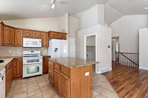 Kitchen featuring white appliances, light stone counters, wood finish cabinetry, lofted ceiling, and track lighting