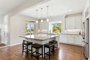 Kitchen with white cabinetry, freestanding refrigerator, a kitchen bar, and a center island with sink