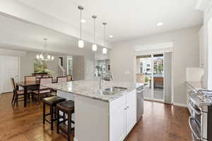 Kitchen with white cabinetry, a center island with sink, stainless steel appliances, light stone countertops, and dark wood-type flooring