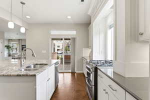 Kitchen featuring stainless steel appliances, white cabinets, light stone counters, and dark wood-type flooring