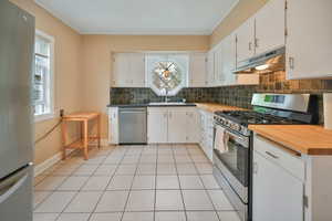 Kitchen featuring stainless steel appliances, white cabinets, tasteful backsplash, butcher block countertops, and tile floors