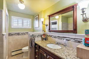 Full bath with a baseboard heating unit, vanity, light tile patterned flooring, tile walls, and wainscoting