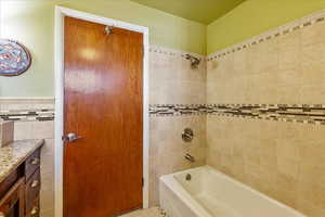 Bathroom with vanity, washtub / shower combination, and tile walls