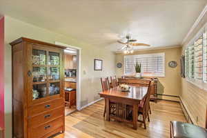 Dining space featuring light wood finished floors, ceiling fan, a baseboard radiator, and plenty of natural light