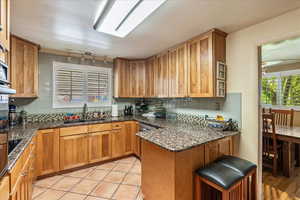 Kitchen featuring dark stone countertops, tasteful backsplash, a peninsula, and wood finish cabinets