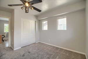 Unfurnished bedroom with an office area, carpet, a closet, ceiling fan, and multiple windows