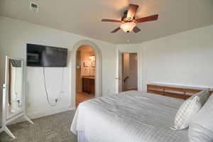 Carpeted bedroom with ceiling fan, arched walkways, and ensuite bathroom