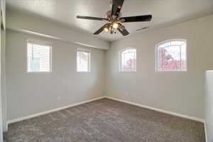 Empty room with dark colored carpet and a ceiling fan