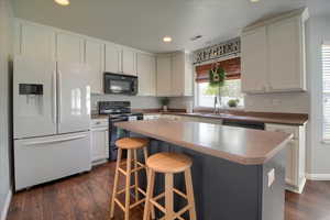 Kitchen featuring black appliances, dark wood finished floors, a kitchen bar, white cabinetry, and recessed lighting