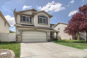 Traditional home with stone siding, a front yard, stucco siding, driveway, and an attached garage