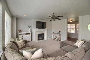 Carpeted living room with a tile fireplace, ceiling fan, and a textured ceiling
