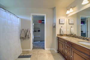 Bathroom with double vanity, a shower with curtain, a spacious closet, and light tile patterned flooring