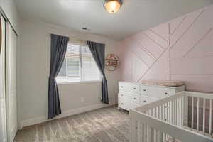 Bedroom with light colored carpet, a nursery area, and a closet
