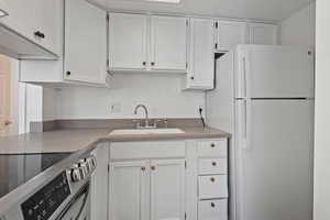 Kitchen featuring freestanding refrigerator, white cabinetry, stainless steel electric stove, and light countertops