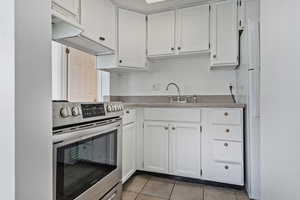 Kitchen featuring electric range, white cabinetry, light tile patterned flooring, freestanding refrigerator, and range hood