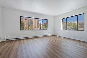 Spare room with baseboard heating, wood finished floors, and healthy amount of natural light