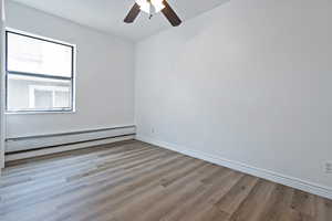 Unfurnished room featuring a baseboard heating unit, ceiling fan, and wood finished floors