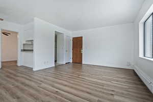 Spare room featuring baseboard heating, light wood-style flooring, and ceiling fan