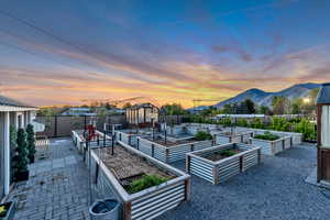 Patio terrace at dusk with a fenced backyard, a patio, a mountain view, and a vegetable garden