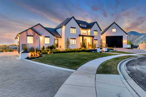 Modern farmhouse featuring decorative driveway, a garage, a lawn, and stucco siding