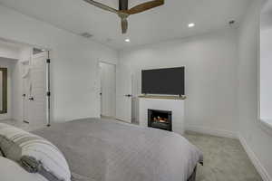 Bedroom with light carpet, recessed lighting, a warm lit fireplace, and ceiling fan