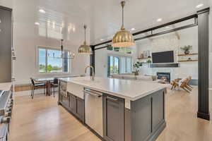 Kitchen featuring light wood-type flooring, open floor plan, hanging light fixtures, stainless steel appliances, and a fireplace