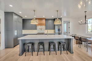 Kitchen with gray cabinets, a breakfast bar area, a large island, light wood-type flooring, and stainless steel double oven