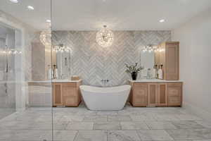 Full bath with tile walls, two vanities, light marble finish flooring, a soaking tub, and a stall shower