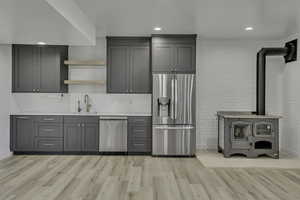 Kitchen with gray cabinets, open shelves, stainless steel appliances, a wood stove, and light wood-type flooring