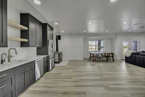 Kitchen with open shelves, open floor plan, stainless steel appliances, light wood finished floors, and decorative backsplash