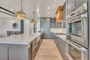 Kitchen featuring stainless steel appliances, decorative light fixtures, gray cabinetry, and a large island
