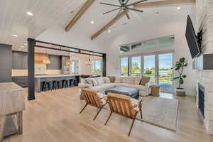 Living room with ceiling fan, light wood-style flooring, a chandelier, a stone fireplace, and lofted ceiling