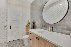 Bathroom featuring tile walls, dark speckled floor, vanity, and backsplash