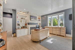 Office space featuring built in shelves, a fireplace, and light wood-style floors