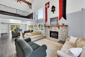 Living area featuring hardwood / wood-style floors, a stone fireplace, a high ceiling, a ceiling fan, and wooden walls