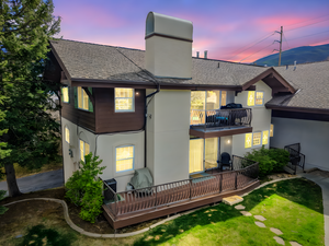 Back of house at dusk with a balcony, a shingled roof, a deck, stucco siding, and a chimney