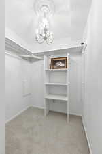 Walk in closet with light colored carpet and a chandelier
