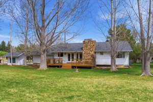 Rear view of property with a chimney, a yard, a deck, and an outbuilding