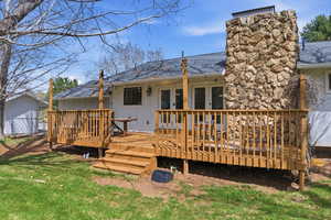 Rear view of house featuring a deck, roof with shingles, a chimney, a lawn, and board and batten siding