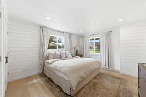 Bedroom featuring wooden walls, light wood-style floors, multiple windows, and recessed lighting