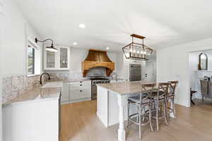 Kitchen with backsplash, light stone counters, white cabinetry, and high quality appliances