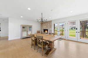 Dining space featuring light wood-type flooring, a stone fireplace, french doors, and recessed lighting