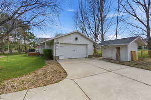 View of side of home with an outdoor structure, an attached garage, roof with shingles, driveway, and board and batten siding