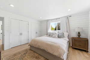 Bedroom with two closets, light wood-style flooring, wooden walls, and recessed lighting