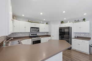 Kitchen with stainless steel appliances, a peninsula, white cabinets, dark wood-style flooring, and dark countertops