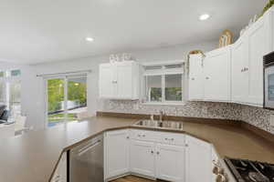 Kitchen featuring white cabinetry, stainless steel appliances, decorative backsplash, recessed lighting, and dark countertops