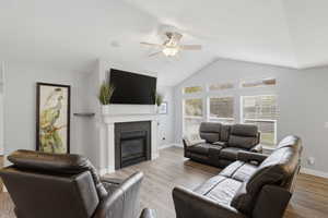 Living room with a ceiling fan, wood finished floors, and a glass covered fireplace