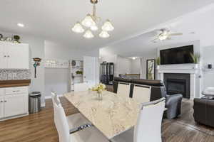 Dining room with ceiling fan, a fireplace, hanging lights, and dark wood-style flooring